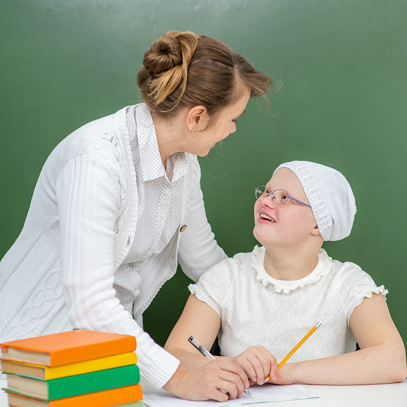 Teacher helps young girl with Down Syndrome at school.